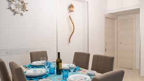 Un comedor con una mesa blanca dispuesta para seis comensales, sillas color beige, una lámpara de techo de madera y un adorno en la pared.