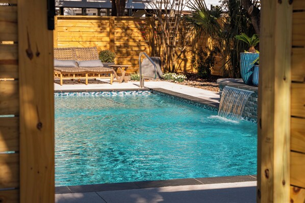 A swimming pool with a waterfall feature, lounge chairs, and a wooden deck.