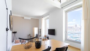 Ett modernt vardagsrum med ett matbord i trä, svarta stolar, en tv och ett stort fönster med utsikt över staden.