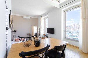 A modern living room with a wooden dining table, black chairs, a TV, and a large window with a city view.