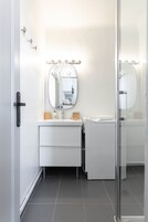 A modern bathroom with a white vanity, a round mirror, and a glass shower enclosure.