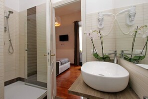 Un bagno moderno con un ampio lavandino bianco, una cabina doccia in vetro e un letto sullo sfondo.