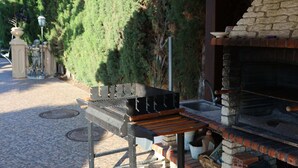 A barbecue grill and sink area with a stone fireplace, surrounded by greenery. - Villa TRES PALMERAS piscina con jacuzzi cerca de Benidorm y Albir (l'Alfàs del Pi)