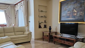 A living room with a beige sofa, a glass coffee table, a TV, and a painting of ships on the wall. - Villa TRES PALMERAS piscina con jacuzzi cerca de Benidorm y Albir (l'Alfàs del Pi)