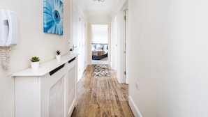 A hallway with a wooden floor, white walls, a blue flower painting, a radiator, and a bed in the distance. - 2 Bed Apartment Sleeps 5 - Free Parking, Balcony (Grays)
