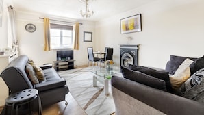 A living room with a sofa, a TV, a fireplace, and a dining area with chairs. - 2 Bed Apartment Sleeps 5 - Free Parking, Balcony (Grays)