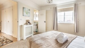 A bedroom with a bed, a bedside table, a window with curtains, a door, and a wall with a picture. - 2 Bed Apartment Sleeps 5 - Free Parking, Balcony (Grays)