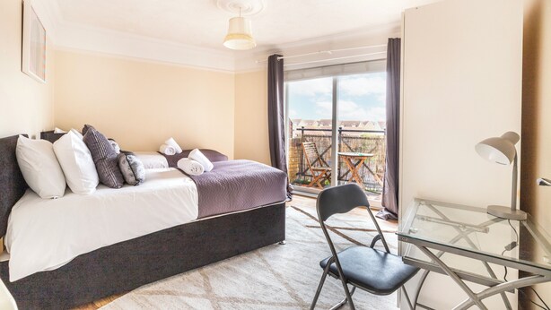 A bedroom with a bed, pillows, a chair, a desk, and a balcony with a view. - 2 Bed Apartment Sleeps 5 - Free Parking, Balcony (Grays)