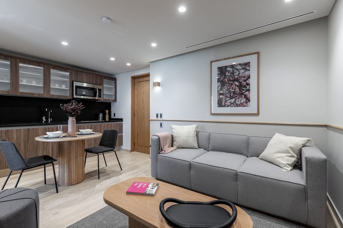 Una sala de estar moderna con un sofá gris, una mesa de centro de madera y un comedor con una mesa redonda y sillas.