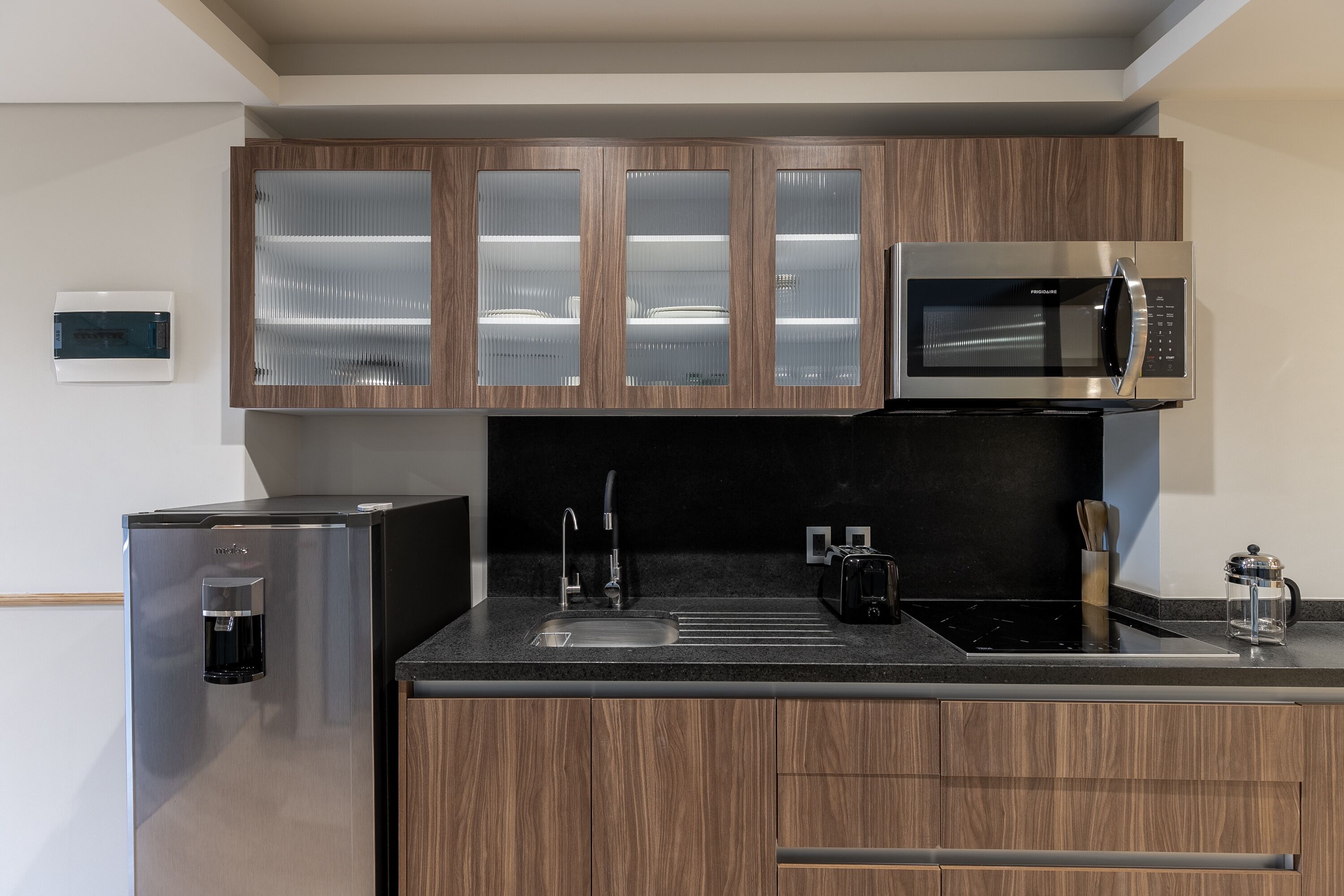 Eine moderne Küche mit Holzausstattung, einem Edelstahlkühlschrank, einer eingebauten Mikrowelle und einer Kaffeemaschine.