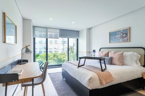 Ein modernes Schlafzimmer mit einem großen Bett, einem Schreibtisch und Blick ins Grüne.