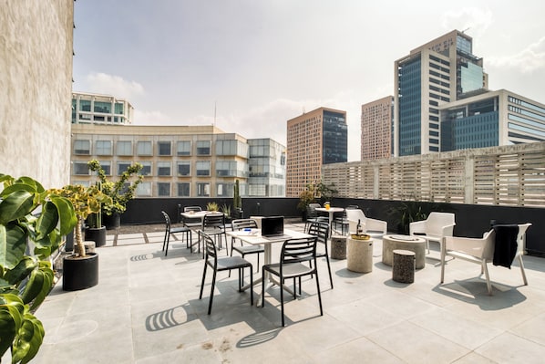 Terraza en la azotea con mobiliario exterior, plantas en macetas y un horizonte urbano al fondo.