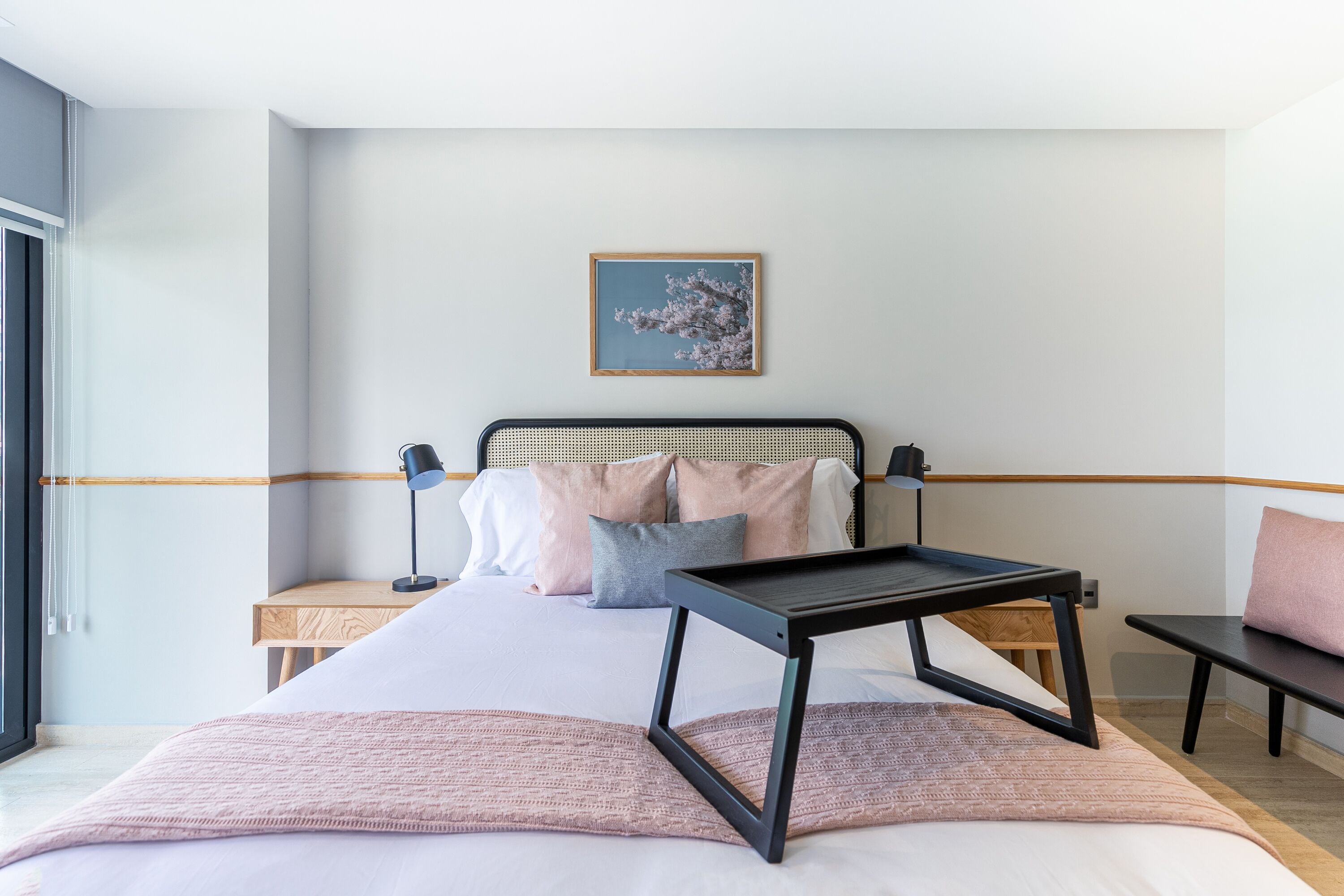 A modern hotel room with a bed, bedside tables, a desk, and a window.