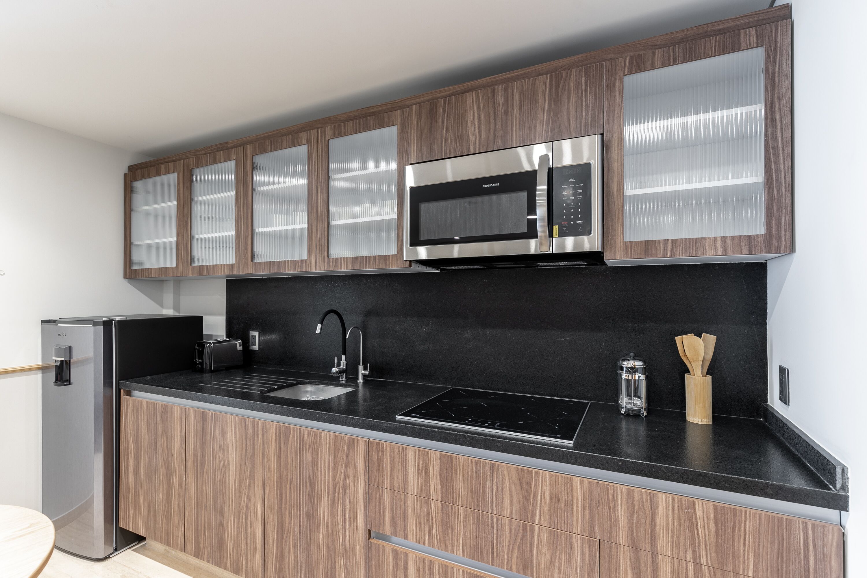 A modern kitchen with wooden cabinets, a stainless steel microwave, a built-in oven, and a black countertop.