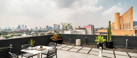 Terraza en la azotea con mesa y sillas, plantas en macetas y vistas al horizonte de la ciudad.