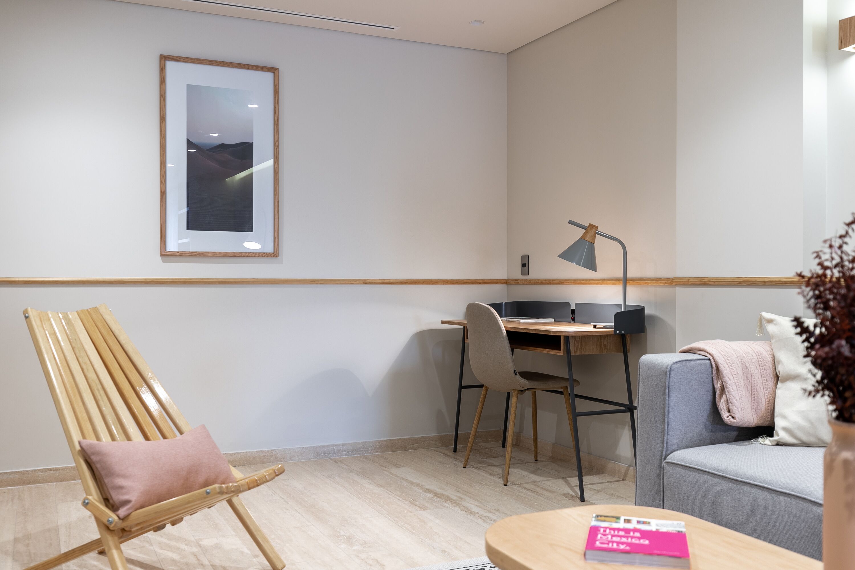 Une pièce moderne avec une chaise en bois, un bureau, un canapé gris et un tableau encadré au mur.