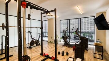 A gym with exercise equipment, a window with blinds, and a plant.