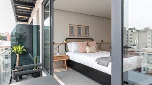 Un dormitorio moderno con cama, mesitas de noche, una planta en maceta y un balcón con barandilla.