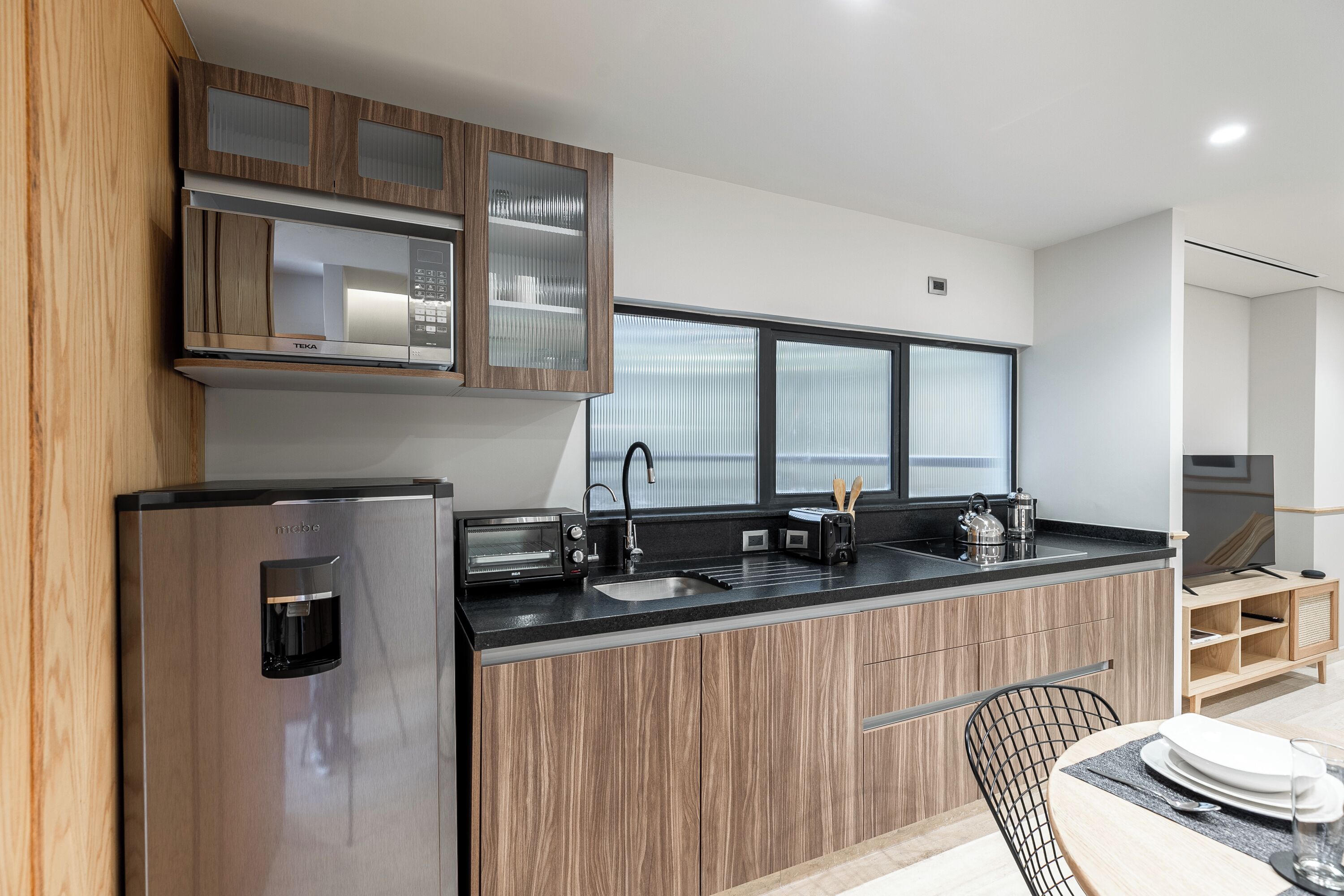 A modern kitchen with a built-in microwave, toaster, and coffee maker, wooden cabinets, and a large window.