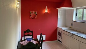 A kitchen with red walls, a dining table with chairs, a stove, and a window.