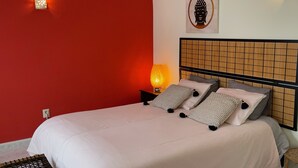 A neatly made bed with white bedding and multiple pillows, a bedside lamp, and a wall-mounted light fixture.