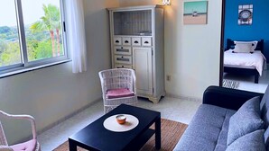 A bedroom with a bed, a white wardrobe, a window with a view of palm trees, a white chair, and a black table with a candle. - The Lemon Tree Villa - Apt. 4 - Algarve/Portugal (Moncarapacho)