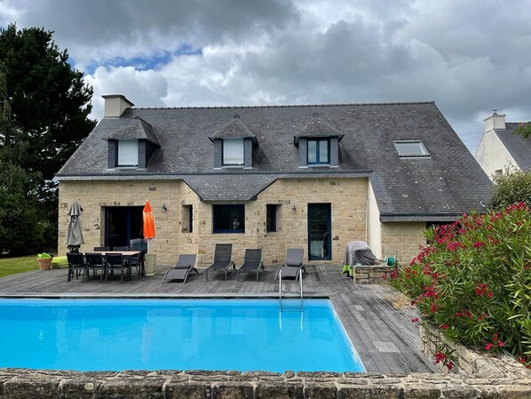 Une maison en pierre avec une piscine, un espace salon extérieur et un jardin fleuri.