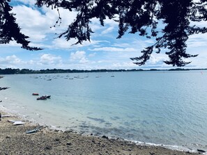 Une plage à l’eau claire, avec des bateaux et une côte rocheuse.