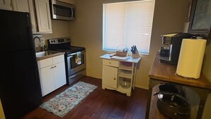 A compact kitchen with a microwave, stove, refrigerator, and a small window with blinds.