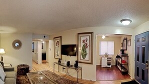 A living room with a sofa, coffee table, and a TV. There is a kitchen area with a sink and cabinets.
