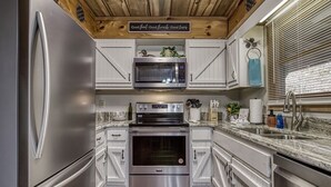 A modern kitchen with stainless steel appliances, white cabinetry, and a wooden ceiling. - Downtown Creekside Cabin~FirePit~Hot Tub~Game Room (Pigeon Forge)