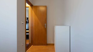 Un corridoio con una porta in legno, un armadietto bianco e uno scorcio di un letto nella stanza successiva.