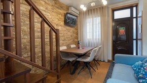 Una stanza con una scala in legno, un tavolo da pranzo con sedie, un divano e una porta con un cartello.