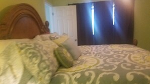 Ett sovrum med en säng, en dörr och ett fönster med gardiner.