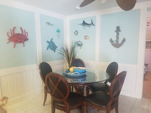 Uma sala de jantar com mesa de vidro cercada por cadeiras de madeira, decorada com quadros de temática marítima.