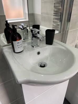 A bathroom sink with a chrome faucet, a soap dispenser, and a black trash bin.