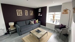A modern living room with a grey sofa, a coffee table, and a side table with a lamp. - The Gateway Apartment 3 (Blackpool)