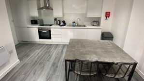 A compact kitchen with white cabinets, a microwave, a stove, and a sink. There is a dining table with chairs and a fire extinguisher on the wall. - The Gateway Apartment 3 (Blackpool)