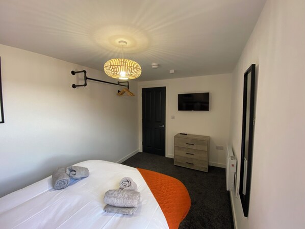 A hotel room with a bed, a television, a wardrobe, and a hanging light fixture.