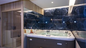 Ein moderner Wellnessbereich mit zwei Whirlpools, Holzliegen und einer gläsernen Sauna.