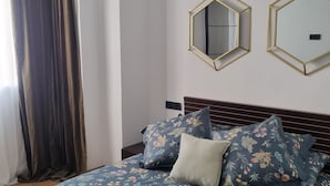 Une chambre à coucher avec une couvre-lit à motifs floraux, deux miroirs hexagonaux et une tête de lit en bois foncé.
