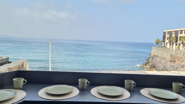 Un balcon avec vue sur l’océan et un bâtiment orné de palmiers.