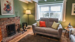 A cozy living room with a fireplace, a sofa, and a large window. - The Cottage (Saltburn-by-the-Sea)