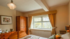 A bedroom with a bed, a wooden wardrobe, a window with curtains, and a chandelier. - The Cottage (Saltburn-by-the-Sea)