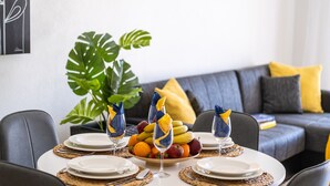 Una mesa de comedor lista, con platos, cubiertos y una cesta de frutas.