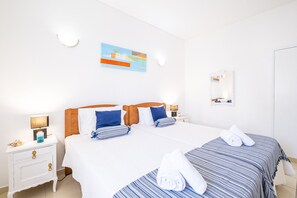 A hotel room with two beds, a nightstand with a lamp, a painting on the wall, and a mirror. - Cozy apartment with pool and BBQ (Albufeira)