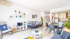 Una sala de estar moderna con un sofá, una mesa de comedor y un televisor. Hay plantas y obras de arte en las paredes.