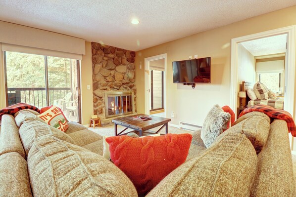 A cozy living room with a stone fireplace, a large flat-screen TV, and a comfortable sofa with a red throw pillow. - New Listing! 2BR/2BA Ski-In/Out Center Village Condo, Indoor Parking-CM216 (Copper Mountain)