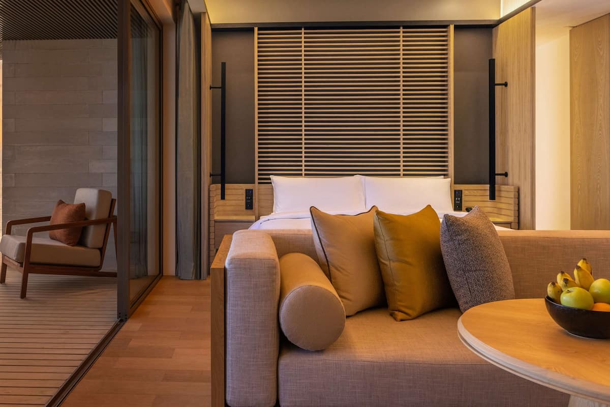 Una habitación moderna con terraza de madera, un sofá con cojines, una mesita con fruta y vistas al mar.