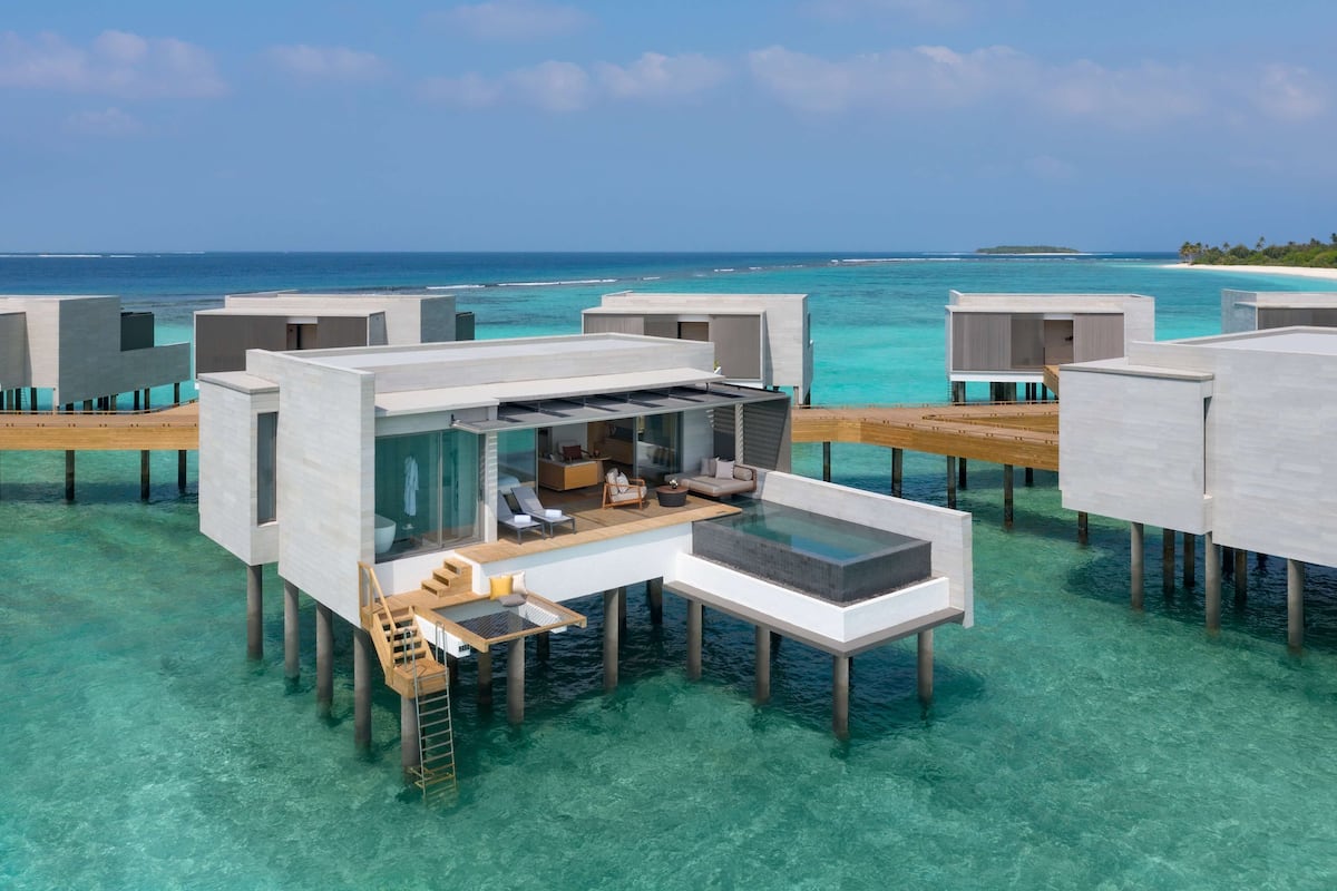 Bungalows sobre el agua con cerramientos de vidrio, terrazas de madera y vistas al océano.